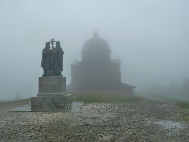 Sousoší sv. Cyrila a Metoděje na vrcholu Radhoště (1129 m.n.m.) před z mlhy vystupující kaplí zasvěcené těmto věrozvěstcům
